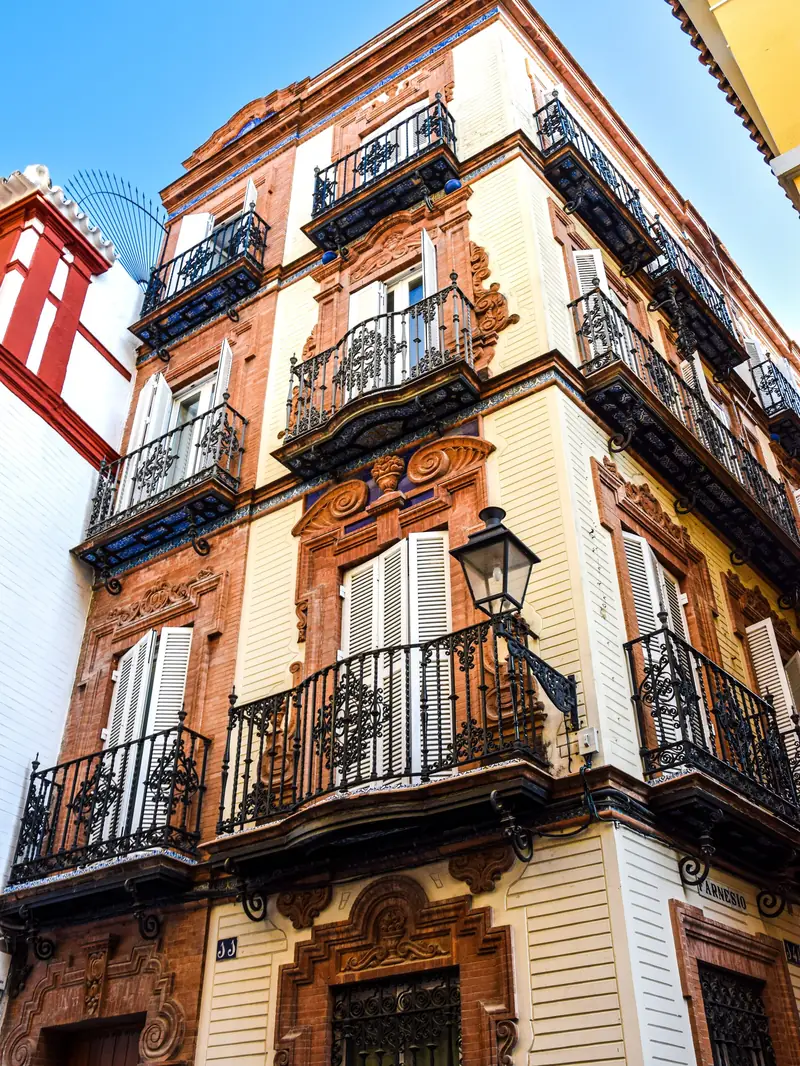 Terracotta and cream townhouse facade with wrought iron balconies on a street corner in Sevilla